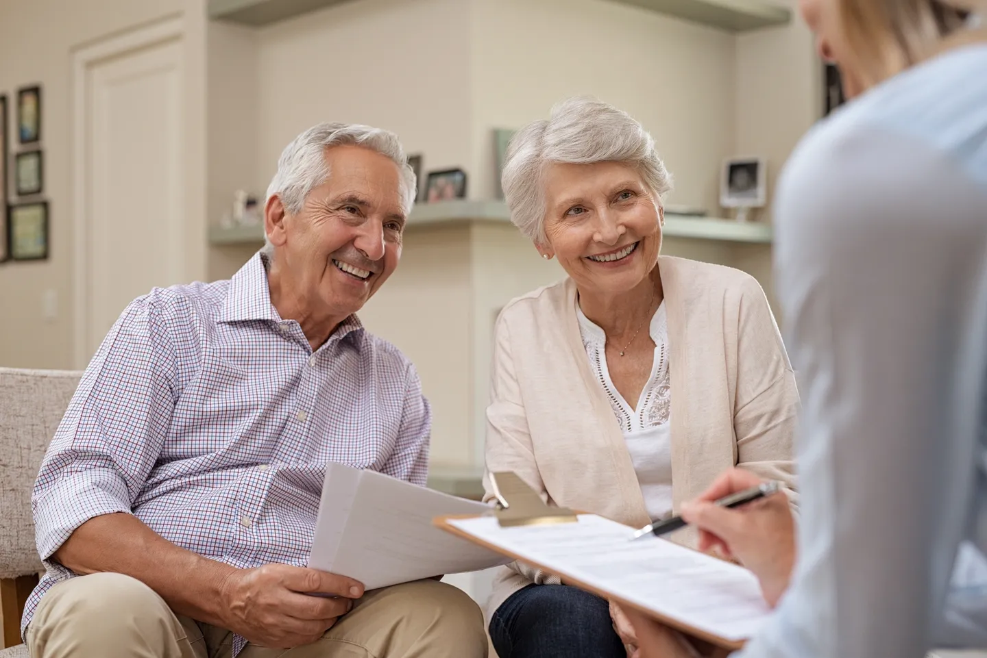 Two older people are smiling while a man is holding papers.